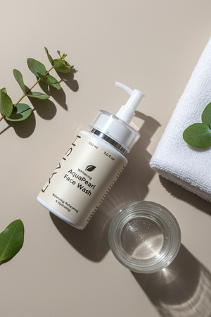 Bottle of Aquascent Face Wash with a pump, glass container, and white towel on a beige background.