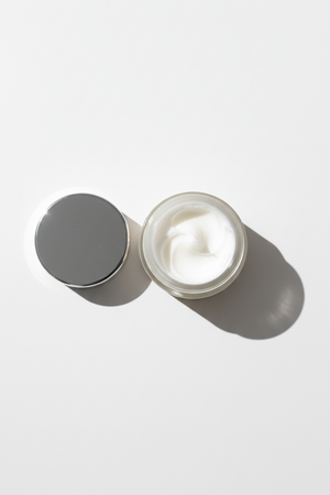 Open jar of cream with a gray lid on a white background