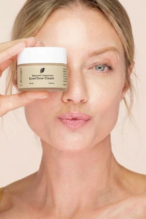 Woman holding a jar of Lavera EvenTone Cream against a beige background