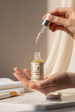 Hand holding a dropper with Lavish Radiance C Serum over a bottle of the serum on a neutral background.